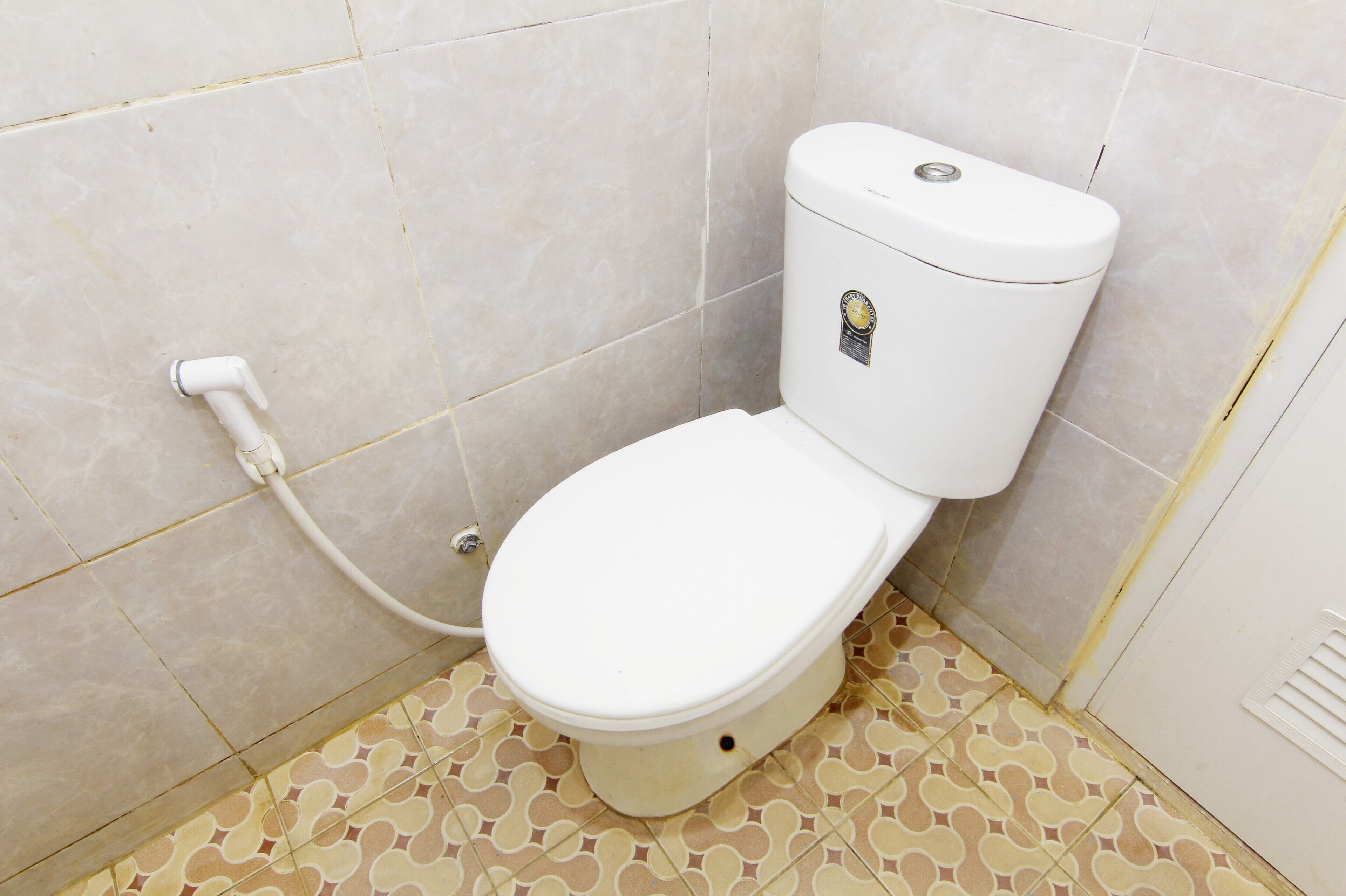 Ein kleines, kompaktes Badezimmer mit Toilette, sichtbarer Wasserleitung und fliesenbelagtem Boden.