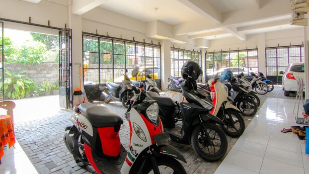 Amplio espacio interior con varias motocicletas estacionadas en filas, grandes ventanales que dejan entrar luz natural y vistas al follaje exterior.