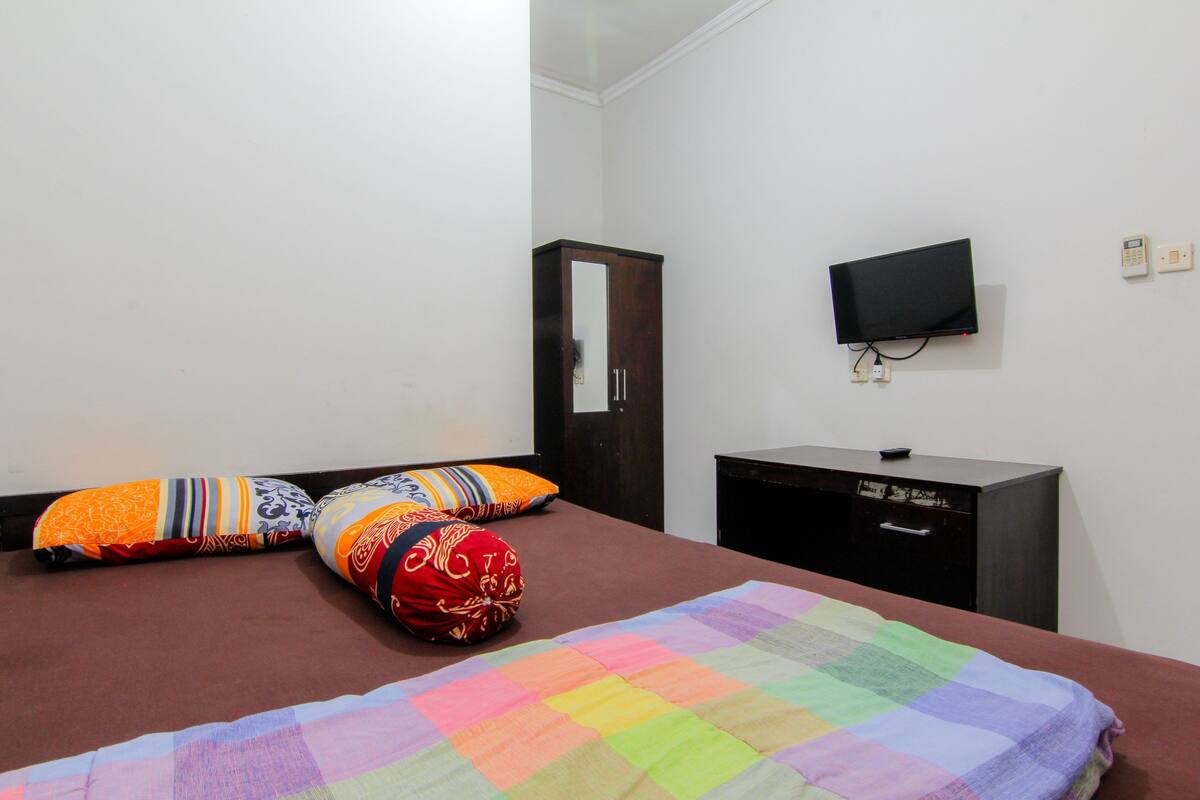 Un dormitorio con cama, almohadas, cómoda, televisor y toma de corriente.