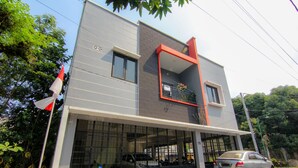 Un edificio moderno de dos pisos con un amplio garaje, un balcón con barandilla roja e izadora con una bandera.