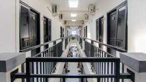 Pasillo de hotel de varios niveles con puertas numeradas 19 y 22, unidades de aire acondicionado y una escalera central.