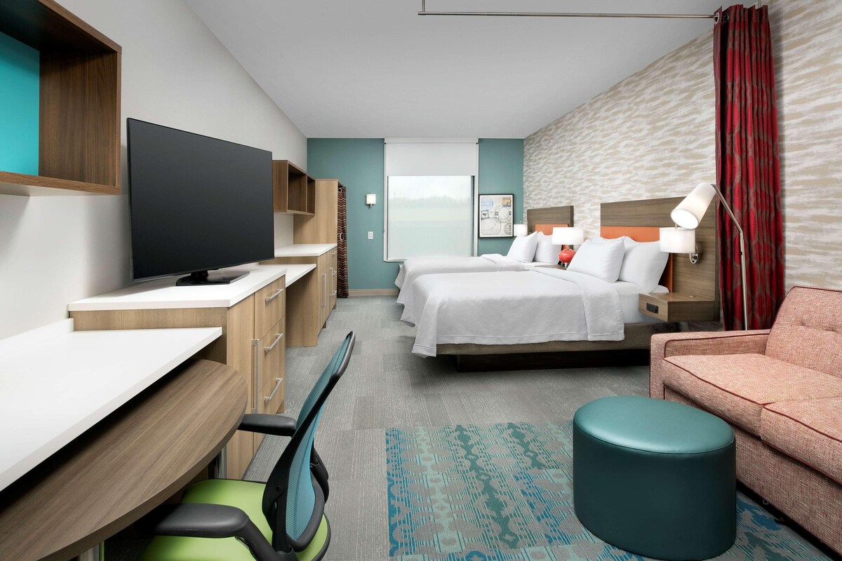 Una habitación de hotel con cama, escritorio, televisor, sofá y un pequeño reposapiés.