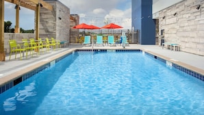 Une piscine dont le bord est recouvert de carrelage, entourée de chaises jaunes et de parasols rouges.