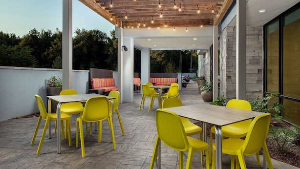 Une terrasse extérieure avec des chaises et des tables jaunes, une pergola illuminée de guirlandes lumineuses et un mur en pierre.