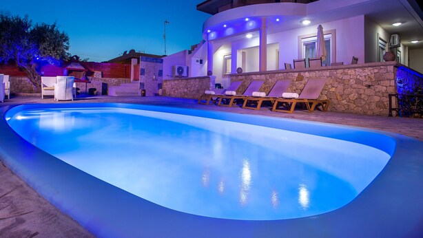 Ein Pool mit Liegestühlen und einer Steinmauer, umgeben von einem Gebäude mit einer Steinaußenfassade und einem überdachten Sitzbereich im Freien.
