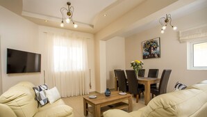 Ein Wohnzimmer mit Fernseher, zwei Sofas, einem Holztisch und einem Esstisch mit Stühlen.