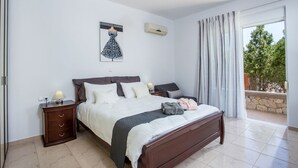 Ein Schlafzimmer mit Bett, Nachttischen, einer Lampe, einer Wand-Klimaanlage und einem fenster mit Vorhängen.