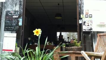 Fachada de La Ferme Gourmande, con una silla de madera y una planta en maceta al frente.