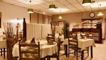 Un restaurante con varias mesas redondas cubiertas con manteles blancos, sillas de madera y lámparas colgantes verdes.