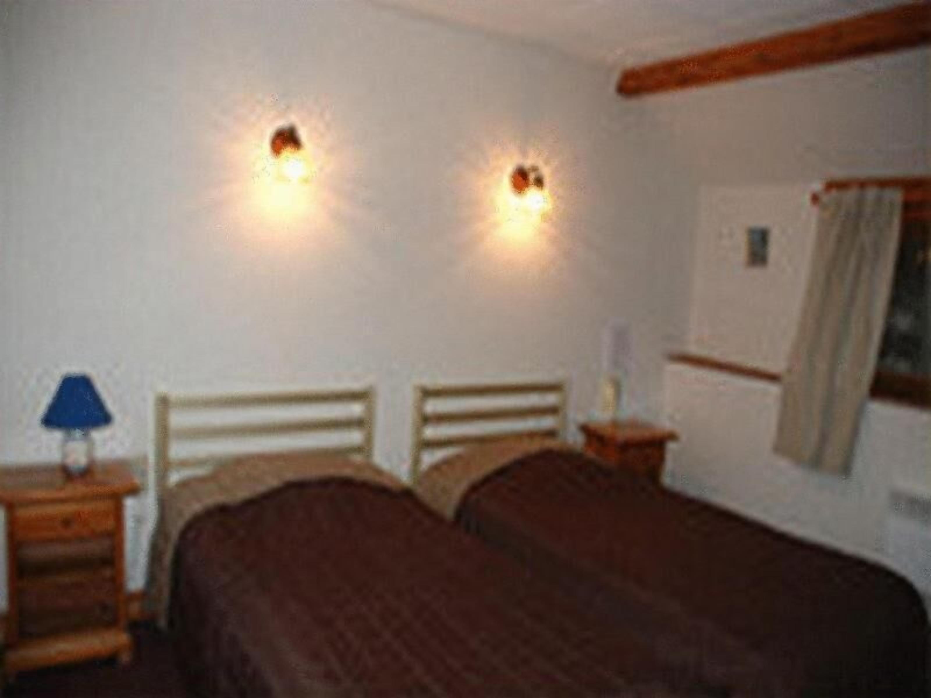 Ein Schlafzimmer mit zwei Betten, einem Nachttisch mit Lampe und zwei Wandleuchten.