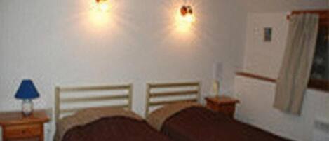 A bedroom with two beds, a nightstand with a lamp, and two wall-mounted lights.