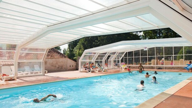 An indoor swimming pool with a glass roof, surrounded by lounge chairs and a poolside area. - Auberge du Colombier (Guines)