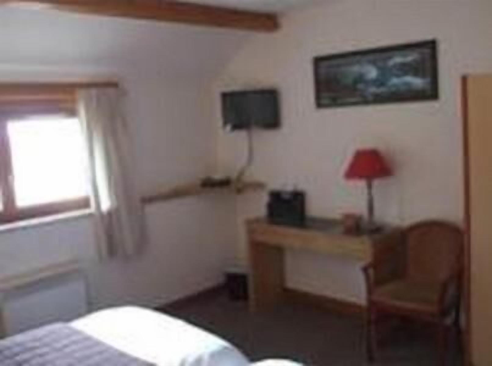 Un dormitorio con cama, escritorio, silla, ventana y un cuadro en la pared.