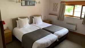 A double bed room with a headboard, bedside tables, a wall-mounted lamp, a window with curtains, and a radiator. - Auberge du Colombier (Guines)