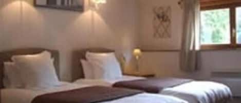 A hotel room with two beds, a nightstand, a lamp, and a window with curtains.