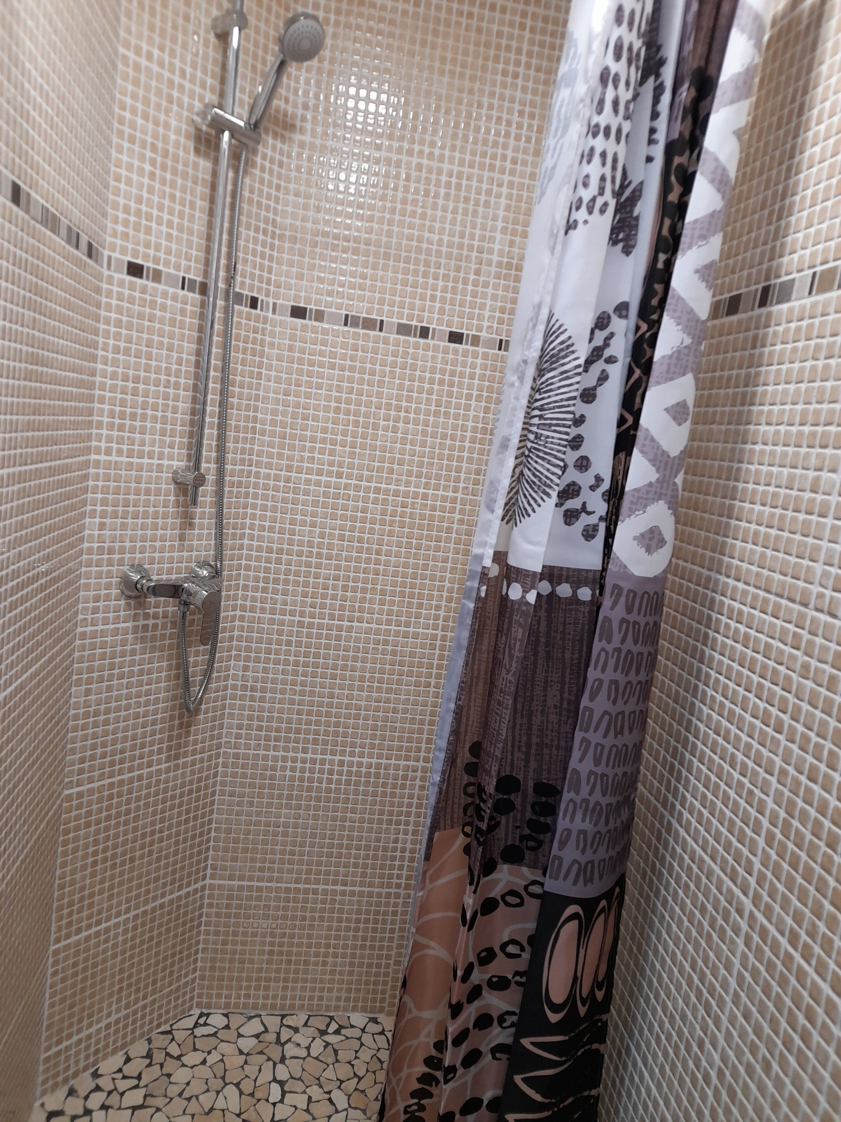 Un espace douche avec un mur carrelé, une pomme de douche et un rideau de douche à motifs.