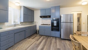 A modern kitchen with grey cabinets, stainless steel appliances, and a wooden dining table. - Beach cottages, majestic Morro Bay (Morro Bay)