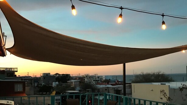 An outdoor patio with a table and chairs, a string of lights, and a view of the cityscape at sunset. - Large Casa in Rocky Point, Mexico (Puerto Peñasco)