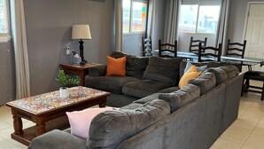 A modern living room with a grey sectional sofa, a wooden coffee table, and a dining area with a table and chairs. - Large Casa in Rocky Point, Mexico (Puerto Peñasco)