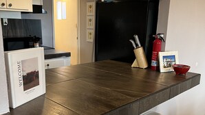 A kitchen with a dark countertop, white stools, a fire extinguisher, and a framed photo on the wall. - Large Casa in Rocky Point, Mexico (Puerto Peñasco)