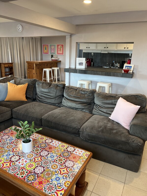 A living room with a dark grey sectional sofa, a colorful patterned coffee table, and a small potted plant.