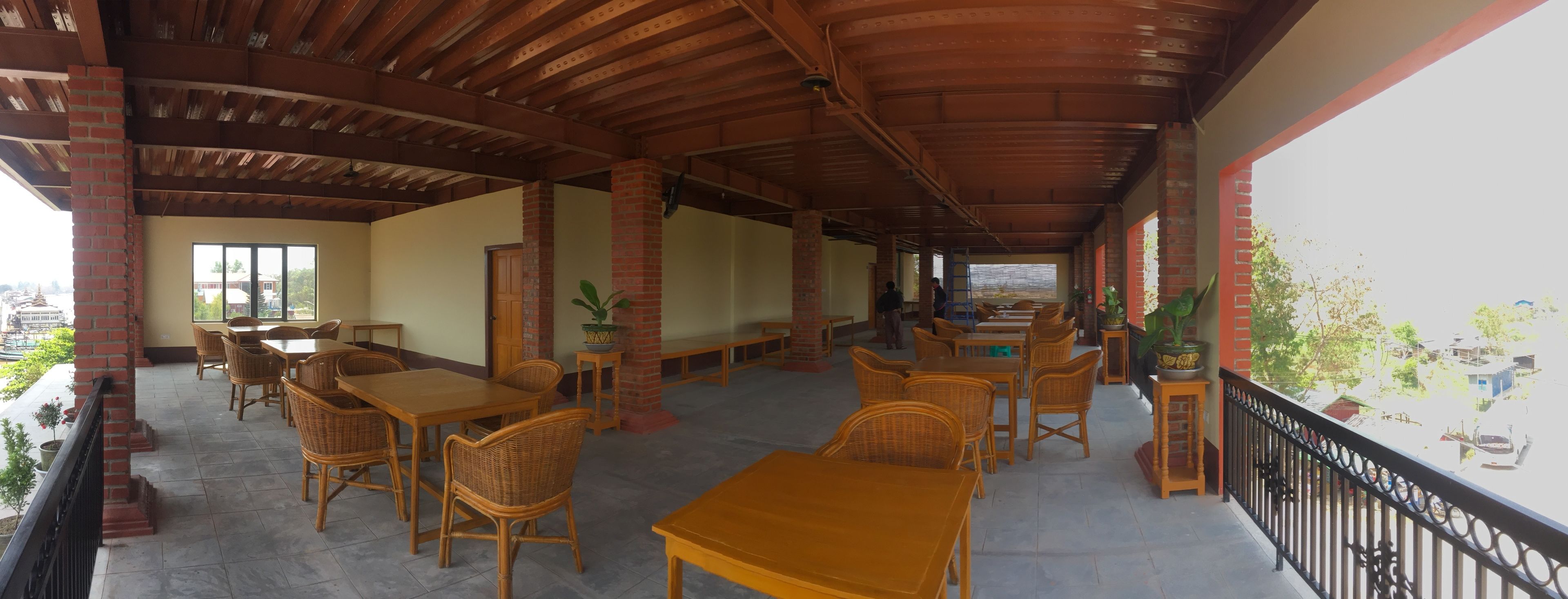 A covered outdoor seating area with tables and wicker chairs, brick pillars, and a view of the city.