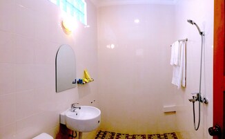 Un baño con lavamanos blanco, espejo, ducha con cabezal de ducha manual y toallero.