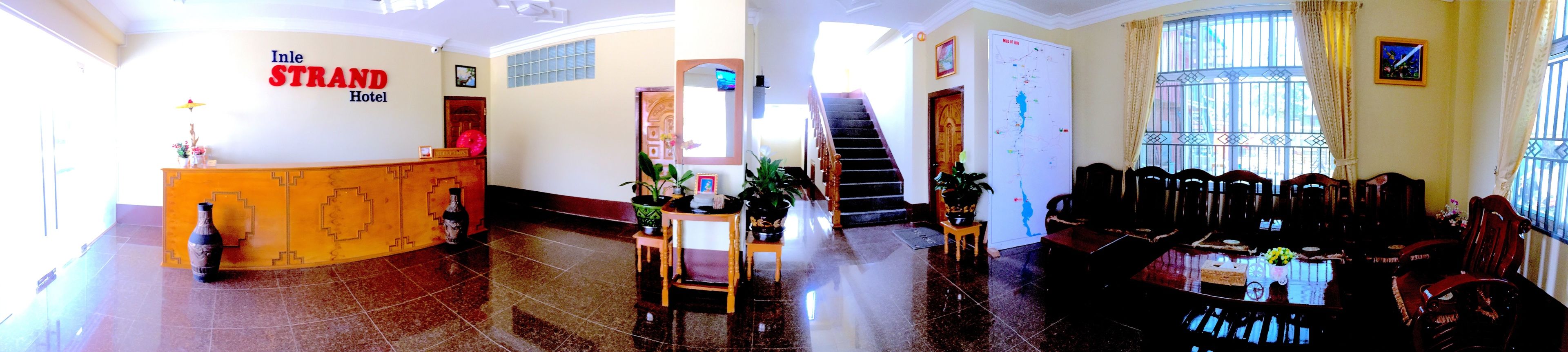 Un vestíbul d'hotel amb una recepció, una escala i una zona de seients amb cadires i una taula.