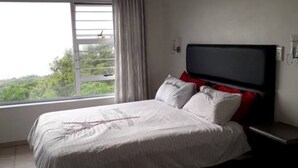 A bedroom with a bed, a ceiling fan, a TV, and a window with curtains. - Shelbourne Sea (Port Shepstone)