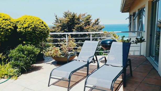 A balcony with two lounge chairs, a grill, and potted plants. - Shelbourne Sea (Port Shepstone)