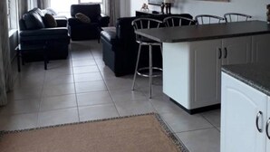A modern living room with a sofa and a dining area with a kitchen counter. - Shelbourne Sea (Port Shepstone)