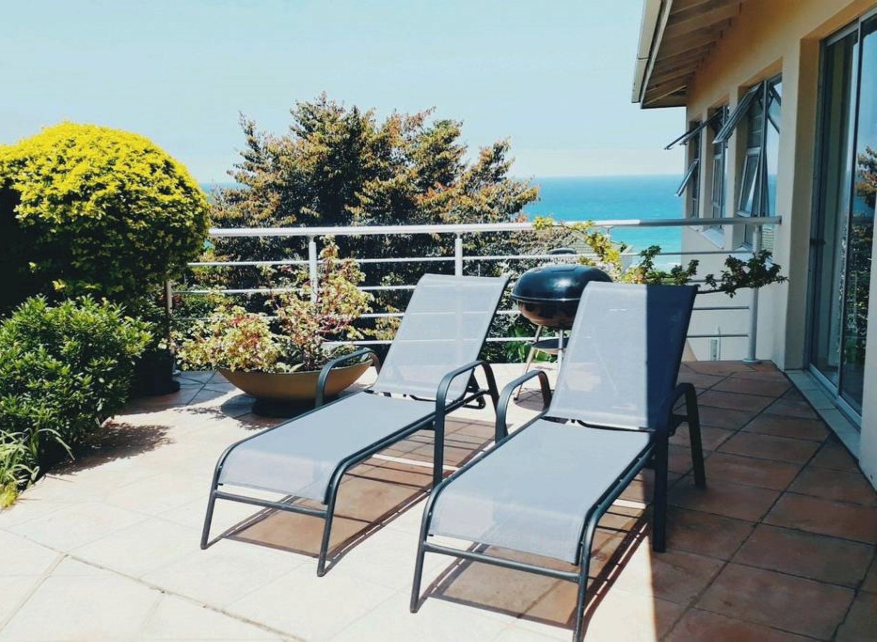 A balcony with two lounge chairs, a grill, and potted plants.