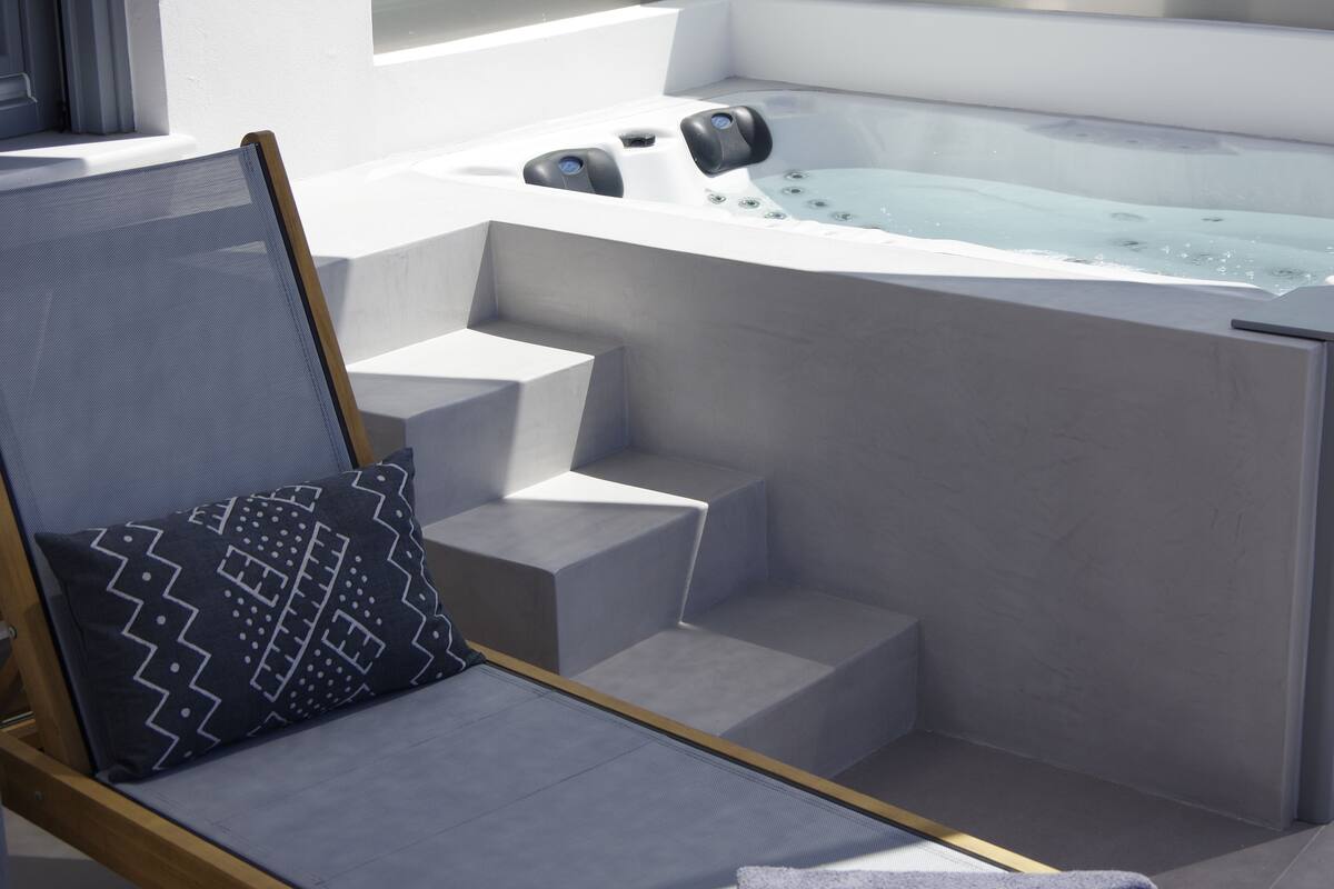 A modern outdoor seating area with a chair and a patterned pillow, a hot tub, and a set of steps leading to it.