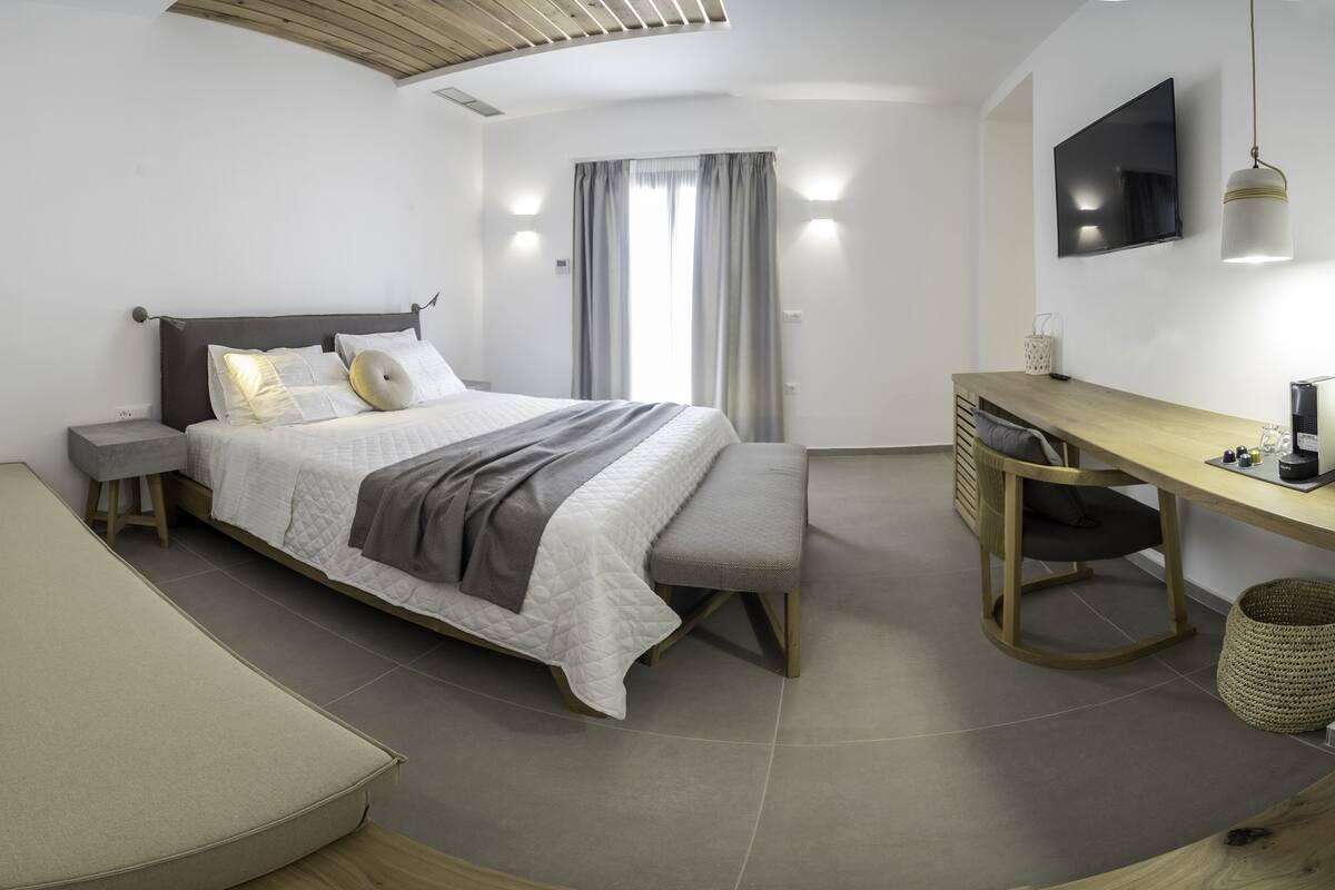A modern bedroom with a bed, bedside table, desk, and a TV.