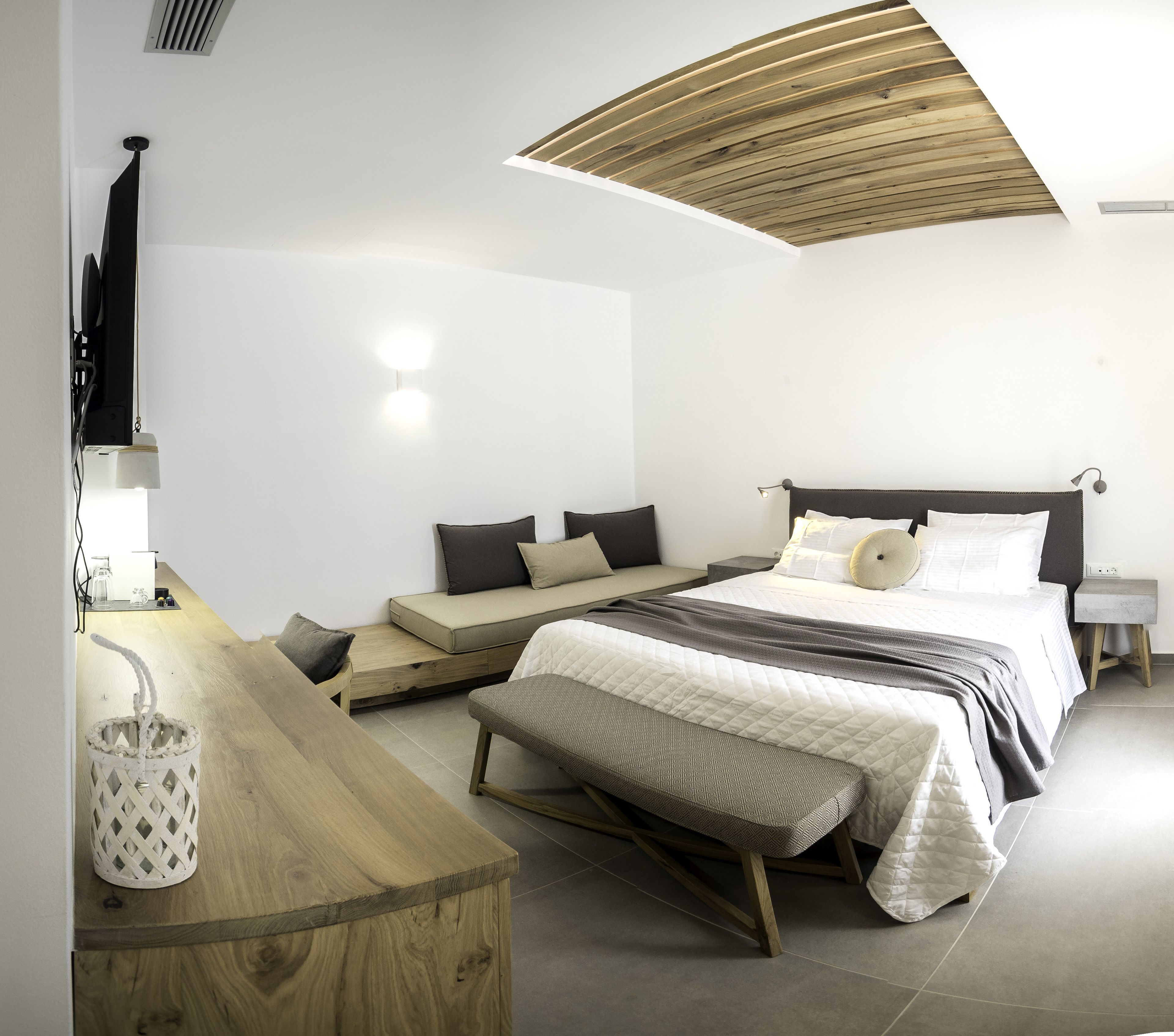 A modern bedroom with a bed, bench seating, and a wooden ceiling.