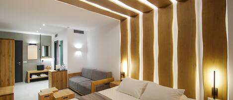 A modern hotel room with a large bed, a sofa, a desk, and a wardrobe.