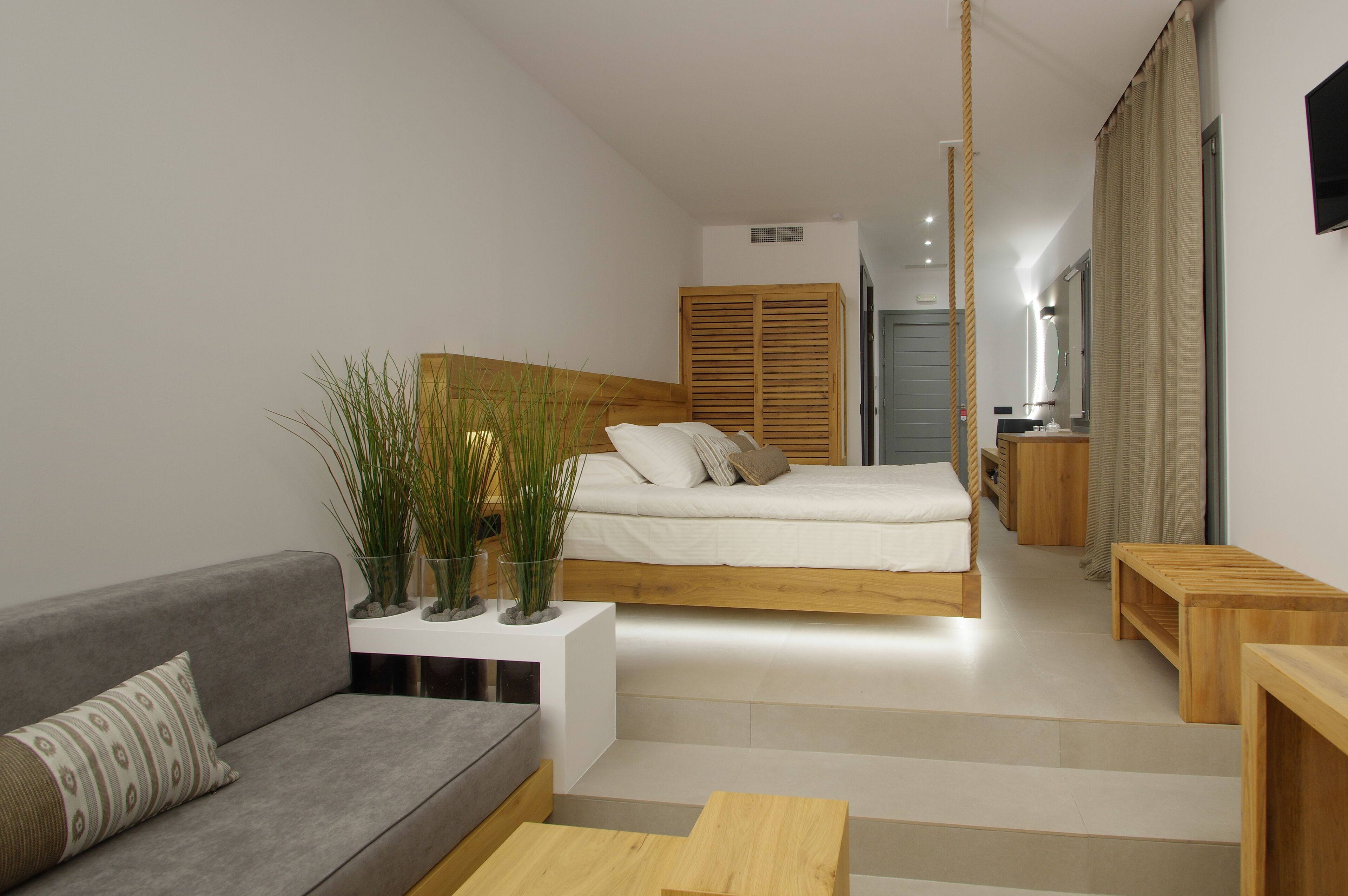 Un dormitorio moderno y minimalista con una cama, un sofá gris y una pequeña mesa de madera.