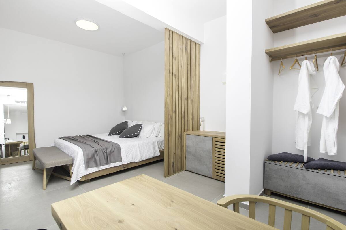A modern, minimalist bedroom with a bed, bedside table, bench, and a wooden wardrobe.