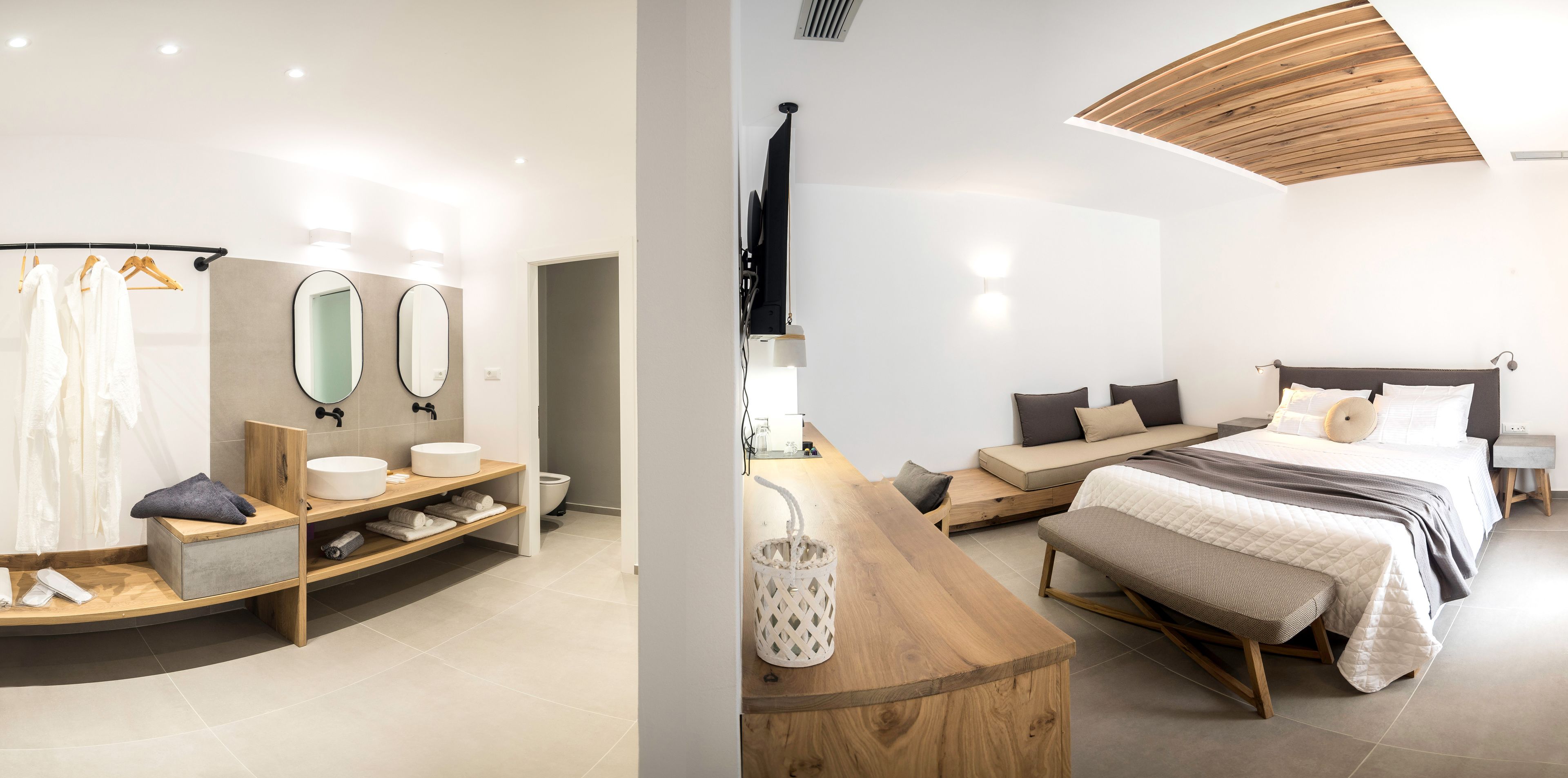 Een moderne badkamer met een gebogen wastafelmeubel, een grote spiegel en een houten bankje. De slaapkamer heeft een bed met een houten hoofdbord, een bankje en een plafond met houten latten.