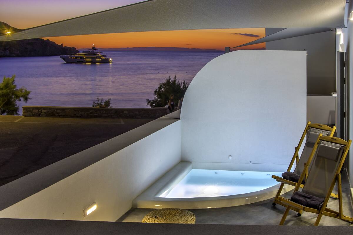 A modern interior with a view of the sea at sunset, a bathtub, and a wooden chair.