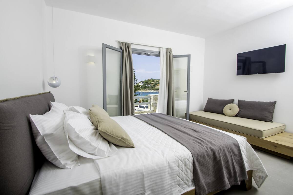 A modern bedroom with a bed, a sofa bed, a TV, and a view of the outside.