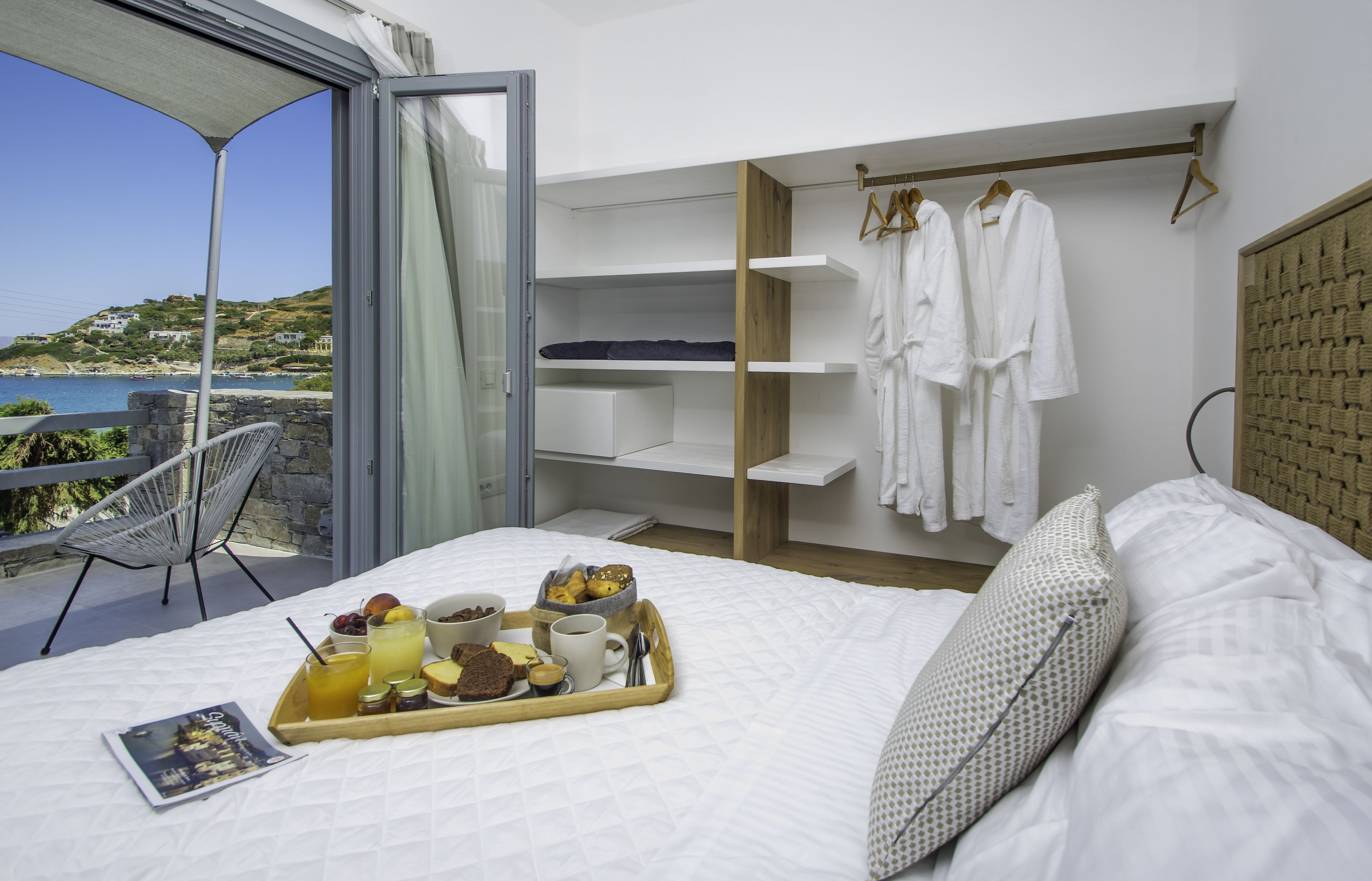 Een slaapkamer met balkon, ontbijttafel en uitzicht op zee.