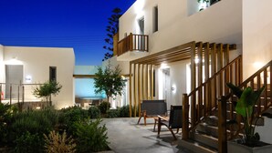 A modern building with a balcony, wooden staircase, and outdoor seating area. - Oro Suites (Syros)