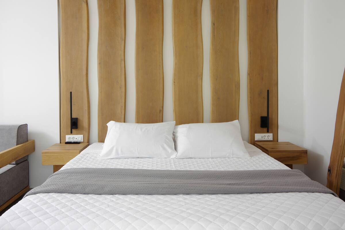 A neatly made bed with white bedding and a gray throw blanket, flanked by wooden headboards and bedside tables with black lamps.