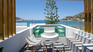 A modern outdoor seating area with a pool, a chair, and a table, overlooking a coastal landscape. - Oro Suites (Syros)