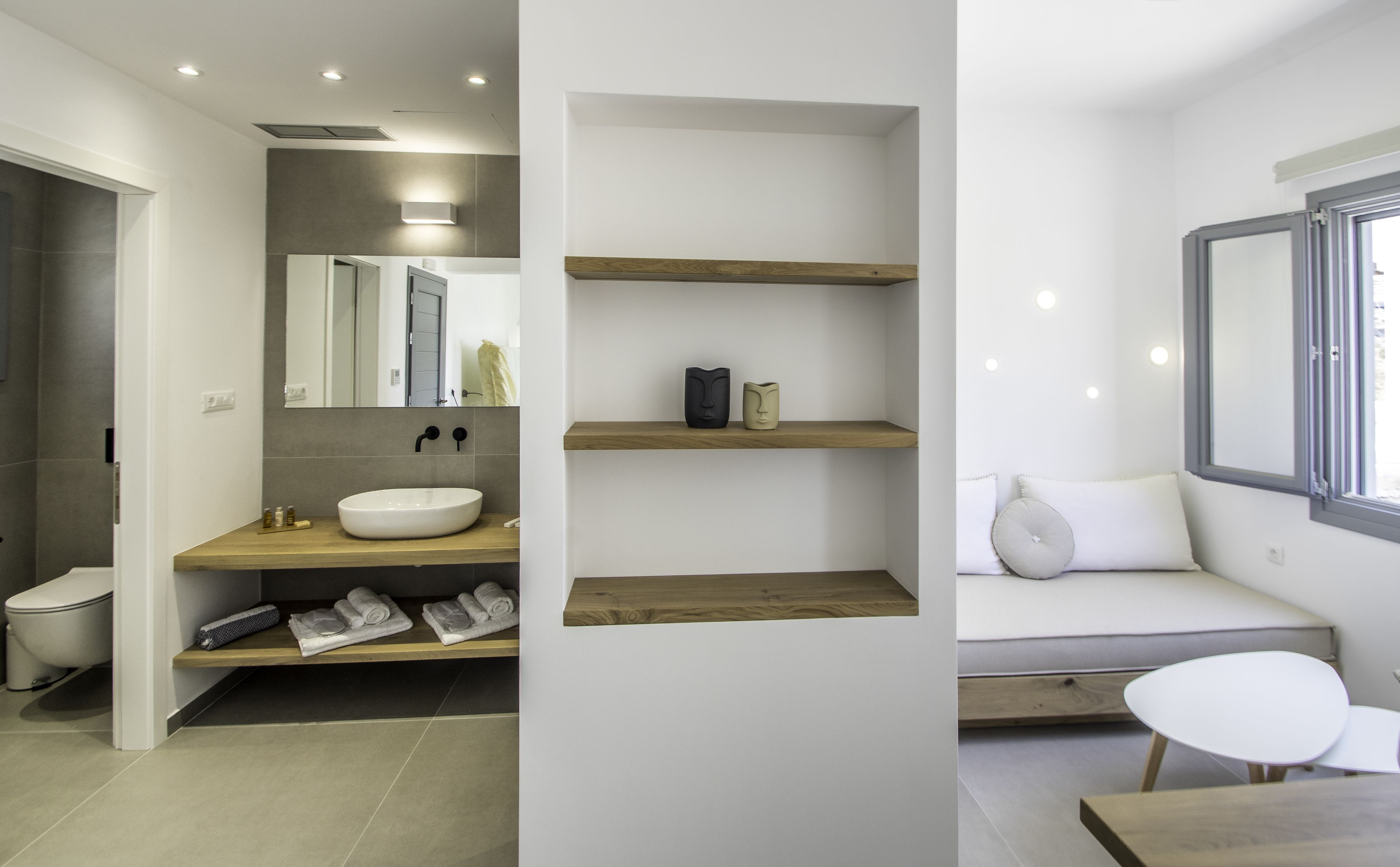 A modern bathroom with a large mirror, a round sink, and wooden shelves.