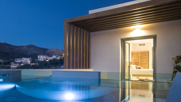 A modern pool area with a clear view of the surrounding landscape and a building entrance. - Oro Suites (Syros)