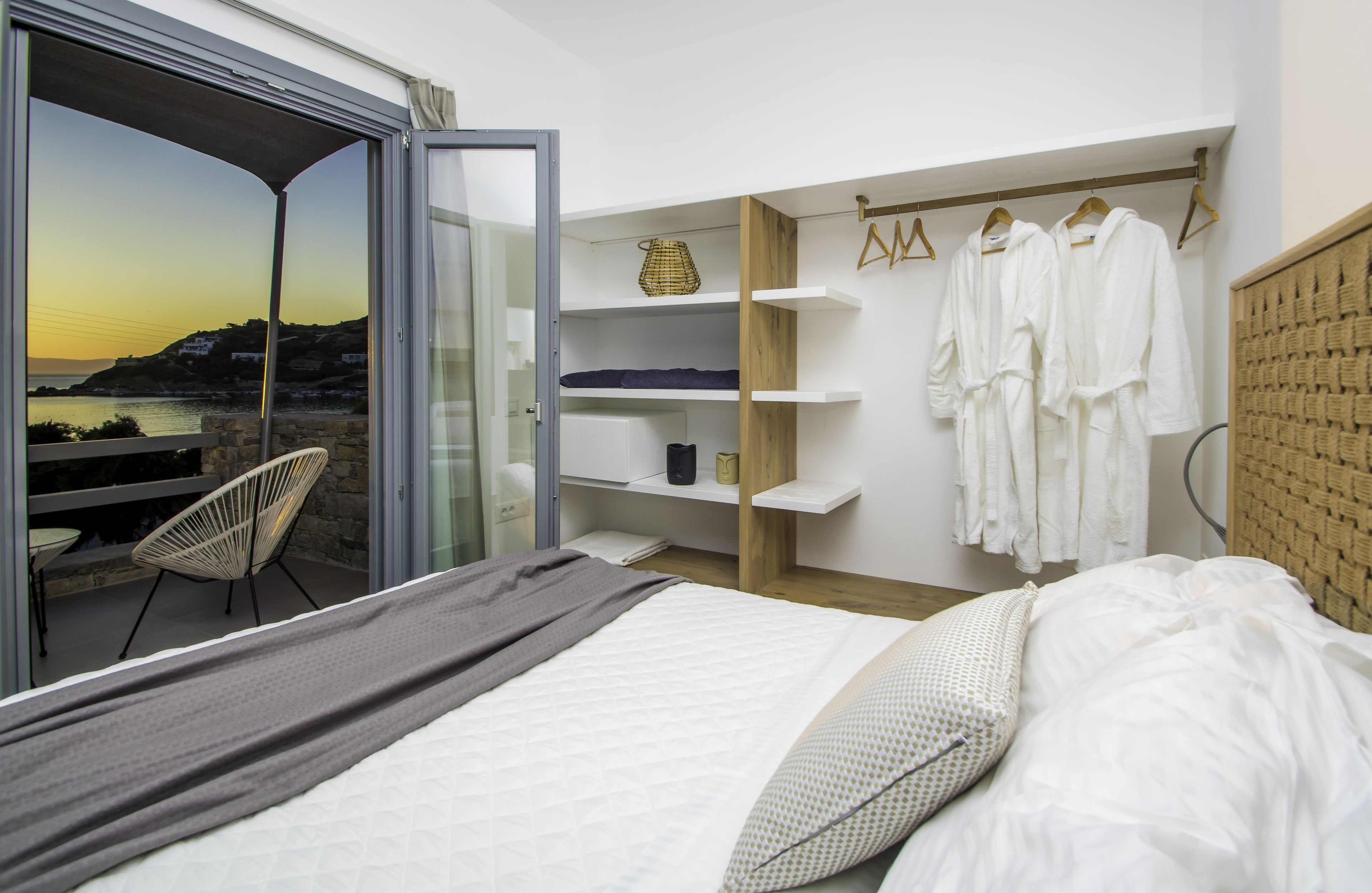 A bedroom with a bed, a chair, a wardrobe, and a view of the sea.