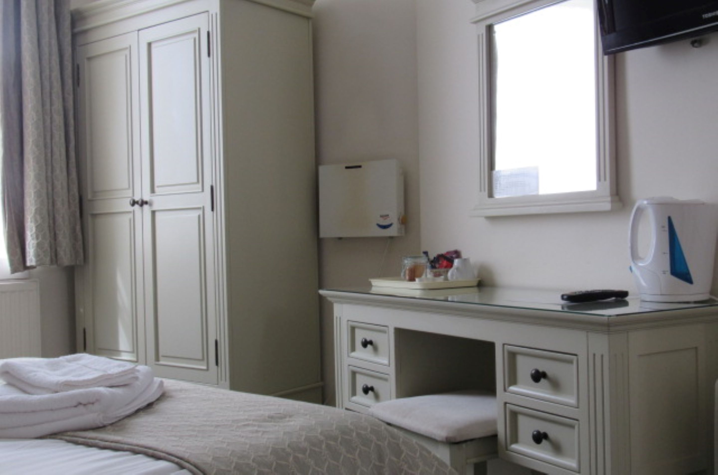Een hotelkamer met een bed, een nachtkastje met een waterkoker, een spiegel en een kledingkast.