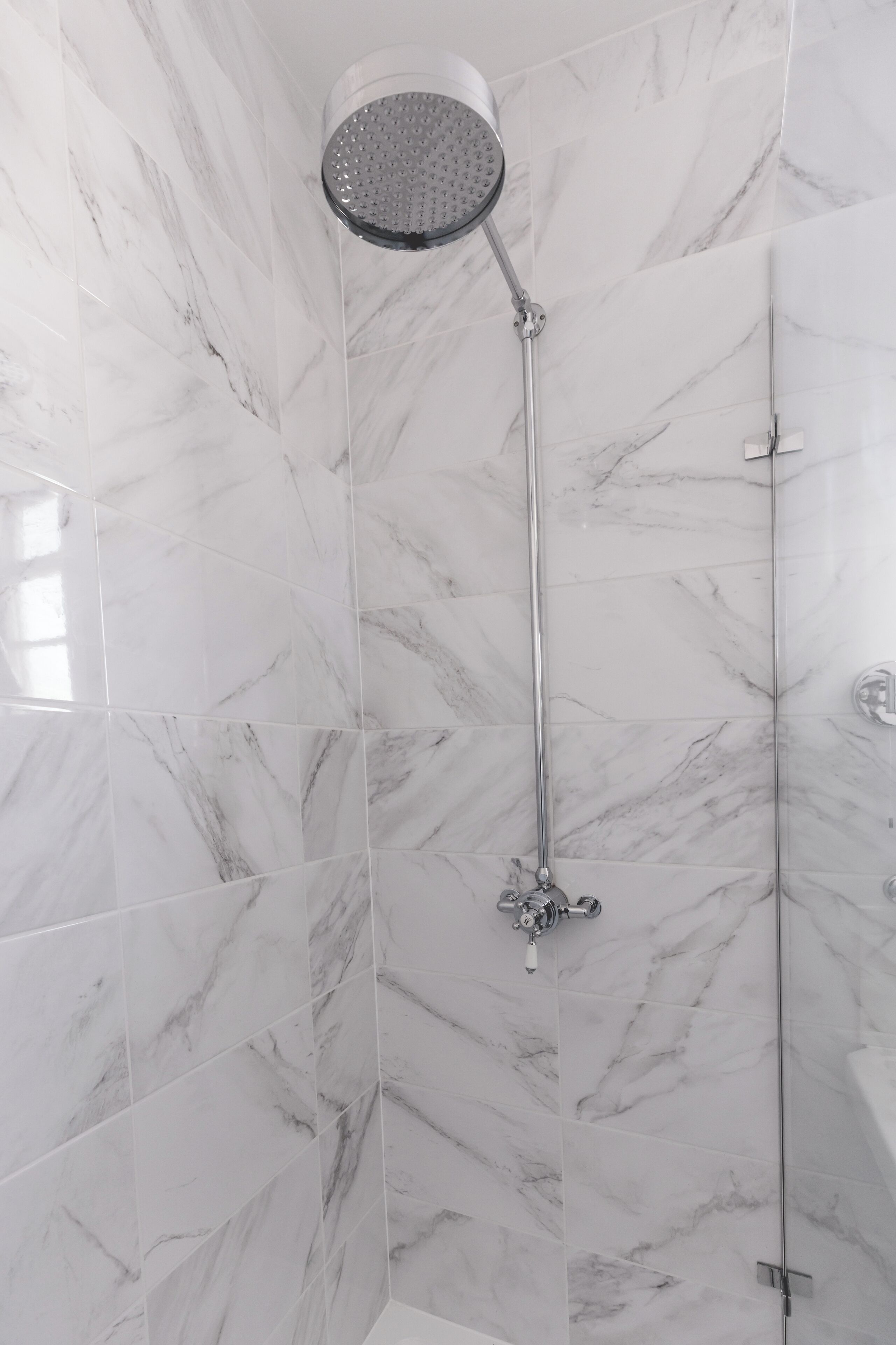 Een moderne badkamer met een douche met glazen wand, marmeren tegels en een zichtbare douchekop.